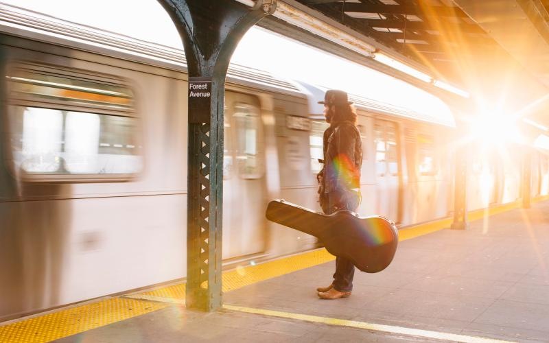 a person waiting on a train while holding a guitar